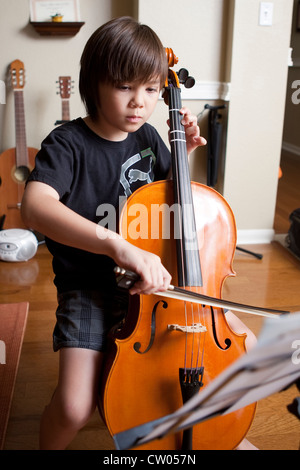 Japanisch-amerikanische 8 jährige junge Praktiken Musikunterricht spielt Cello und Noten lesen, während zu Hause Stockfoto