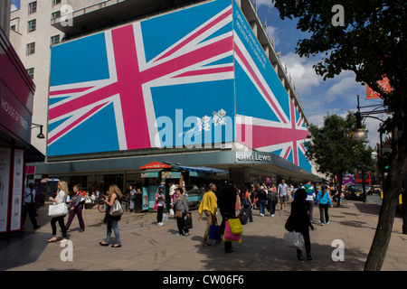 Londoner Verkehr fahren Sie unter einer riesigen Plakatwand Wandbild umwickelt das äußere der John Lewis Department Store in der Oxford Street im Zentrum von London, während der Olympischen Spiele 2012 in London. Im Rahmen ihrer Partnerschaft mit dem Londoner Organisationskomitee für die Olympischen und Paralympischen Spiele (LOCOG), John Lewis arbeiten mit ihren Partnern Gelegenheit am LOCOG und im Vorfeld der Spiele arbeiten Ausstattung Lounge und Rezeption Bereiche im Spiele-Locations. Stockfoto