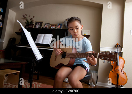 Japanisch-amerikanische 10 Jahre alten Mädchen übt Gitarre spielen, Noten, während zu Hause verwendet. Stockfoto