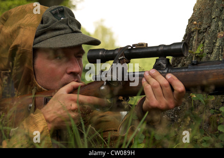 Mann in Form von Nazi-Scharfschütze Ziele in der Nähe eines Baumes Stockfoto