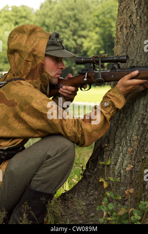 Mann in Form von Nazi-Scharfschütze Ziele in der Nähe eines Baumes Stockfoto