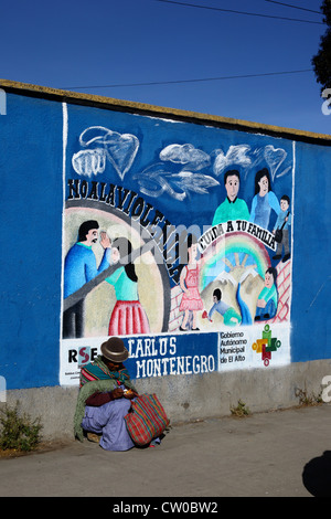 Die gebürtige Frau sitzt auf dem Bürgersteig neben einem Wandgemälde, das Teil einer Kampagne zur Reduzierung von häuslicher Gewalt gegen Frauen ist, El Alto, Bolivien Stockfoto