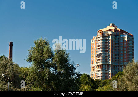 Gebäude und Schornstein, zwischen den grünen gegen den blauen Himmel. Stockfoto