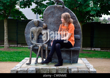 Hübsches junges Mädchen sitzt auf einem Bronze zweisitzersofa, mit einem Herzen zurück geformt, in einem öffentlichen Park in Neufchatel en Bray, im nördlichen Frankreich, Europa. Stockfoto