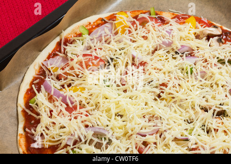 Rohen ungekochten Pizza mit Schinken, Tomaten und Gemüse auf ein Backblech legen, close-up als Draufsicht für italienisches Essen Stockfoto