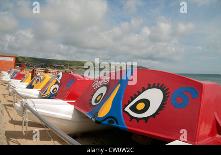 Eine Reihe von farbenfrohen Tretboote am Strand neben der Promenade in Swanage Bay, Dorset, UK. Stockfoto