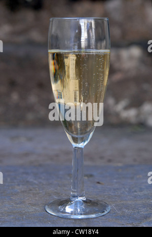 Ein Glas Champagner auf einen Garten Schritt bei einer goldenen Hochzeitsfeier.  Ein Haus spiegelt sich im Glas. Stockfoto