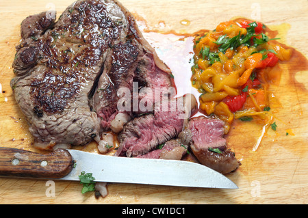 Eine Pfanne angebraten Rumpsteak wird in Scheiben geschnitten auf einem Brett mit gehackte eingelegte Paprika und Petersilie Stockfoto