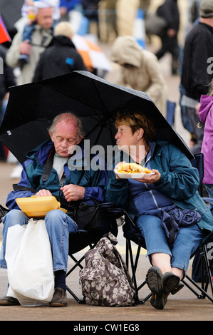 Paar genießt Fish &amp; Chips unter einem Regenschirm bei einer Veranstaltung Stockfoto