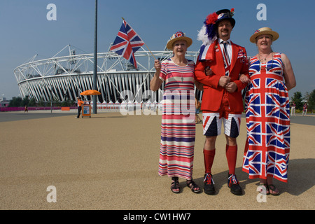 Ein großer Sohn in der Mitte begleitet seine Mutter (l) und Schwester (R) im Olympiapark während der Olympischen Spiele 2012 in London. Union Jack Entwürfe tragen Kleider und Shorts sowie eine Krawatte und Flagge, Welle, das Trio stehen vor dem wichtigsten Olympiastadion bevor die großen Massen im Laufe des Tages ankommen. Sie haben Tickets zu beobachten die Hockey und stehen als exzentrische Briten tragen ihre Nationalfarben lächelnd. Stockfoto