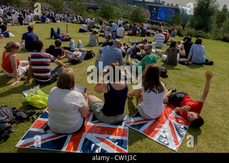 Briten genießen Sie einen heißen Sommer zu beobachten live-Boxen Berichterstattung aus einem großen tv-Bildschirm im Olympiapark während der Olympischen Spiele 2012 in London. Auf Union Jack-Flaggen sitzen, sitzen sie auf dem grünen Rasen liegt auf einem Hügel. Londoner Olympiapark, in knapp einer Quadratmeile ist der größte neue Park in der Stadt seit mehr als 100 Jahren. Die Anpflanzung von 4.000 Bäume, 300.000 Feuchtgebietspflanzen und mehr als 150.000 Stauden sowie nektarreichen Wildblumen sorgen für eine farbenfrohe Kulisse für die Spiele. (Weitere Beschriftungen in Beschreibung...) Stockfoto