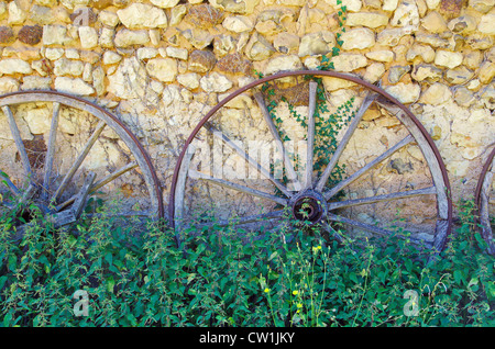 Alte Wagen-Räder und Brennesseln gegen Steinmauer Farm in Frankreich Stockfoto