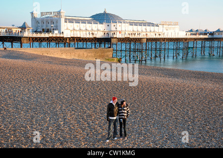 Zwei Teenager stehen auf einem leeren Brighton Beach, mit dem warmen Winter Licht leuchten auf dem nahe gelegenen Pier. East Sussex, England, UK. Stockfoto