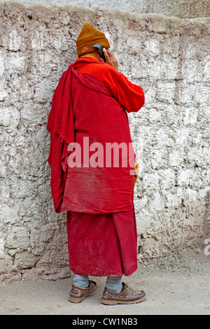 Ein Mönch, in den traditionellen roten Roben tragen ein Vlies Nike Hut auf seinem Handy im Hemis Kloster, Ladakh, Indien sprechen. Stockfoto