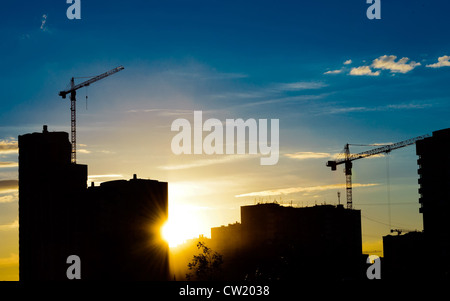 Industrielle Baukräne und Gebäude Silhouetten über Sonne bei Sonnenaufgang Stockfoto