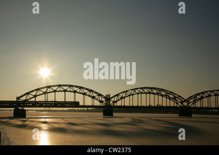 Zug der Stahl gewölbte Eisenbahn-Brücke über den gefrorenen Fluss Daugava, Riga, Lettland Stockfoto