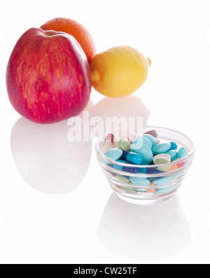 Konzept der Vitamin-Medizin mit verschiedenen Pillen in Glasschale und defokussierten Früchten auf Hintergrund mit weichen Schatten Stockfoto