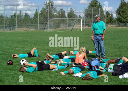 Die männlichen Fußball-Trainer gibt eine Pep Talk, während ein junges Mädchen-Team auf dem Feld zwischen außerschulischen Fußballspiele in Bend, Oregon, USA ruht. Stockfoto