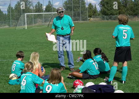 Der männlichen Trainer gibt eine Pep Talk, während ein junges Mädchen-Team auf dem Spielfeld zwischen außerschulischen Fußballspiele in Bend, Oregon, USA ruht. Stockfoto