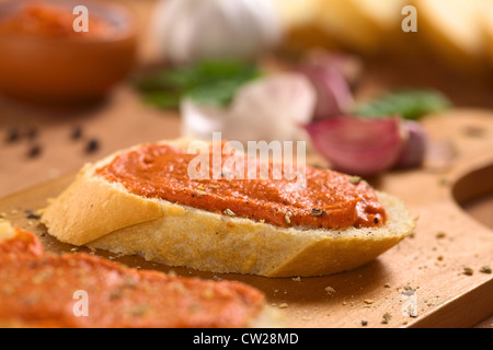 Hausgemachte Tomaten-Butter verteilt auf Baguette Scheiben mit frisch gemahlenem Pfeffer auf Holzbrett Stockfoto