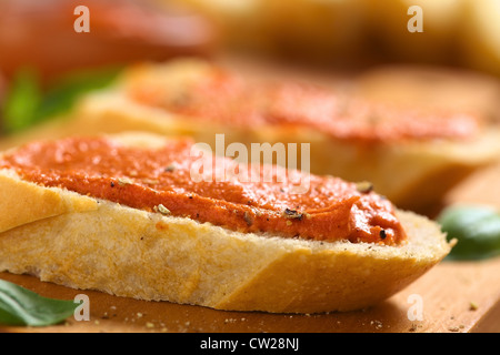 Hausgemachte Tomaten-Butter verteilt auf Baguette Scheiben mit frisch gemahlenem Pfeffer auf Holzbrett Stockfoto