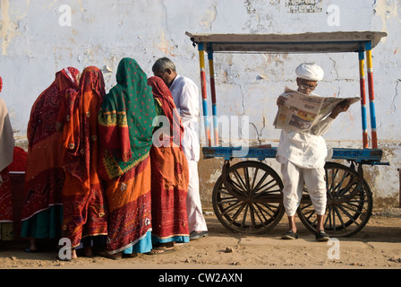 Älterer Mann lesen Zeitung. Rajasthani Frauen Einkaufen für Farbe Farbstoffe neben - Pushkar, Rajasthan. Stockfoto