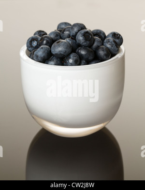 Weißes Glastasse voll von blauen Heidelbeeren glänzende gradient Oberfläche reflektieren Stockfoto