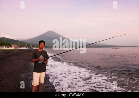 Bei Sonnenaufgang Fische ein lächelnder balinesische jungen zum Frühstück mit dem heiligen Vulkan Gunung Agung, im Hintergrund. Stockfoto