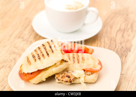 Geröstetes Huhn, Tomaten und Mozzarella Panini Sandwich, das in zwei Hälften geschnitten und auf eine Platte gelegt wurde Stockfoto