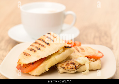 Geröstetes Huhn, Tomaten und Mozzarella Panini Sandwich, das in zwei Hälften geschnitten und auf eine Platte gelegt wurde Stockfoto