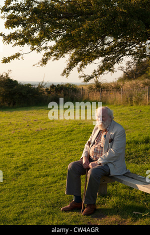 Älterer Herr saß auf der Bank im Landschaftspark, die Abendsonne genießen Stockfoto