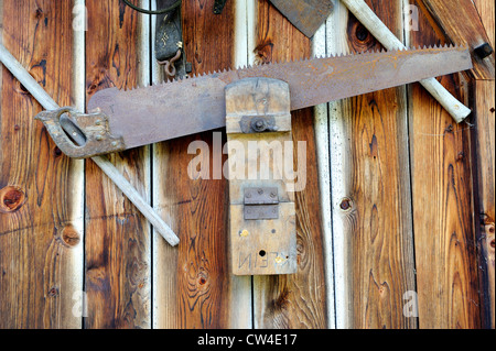 Alte Werkzeuge für die Holzbearbeitung und landwirtschaftliche Geräte fest an der Seite einer hölzernen Scheune in den österreichischen Alpen. Stockfoto