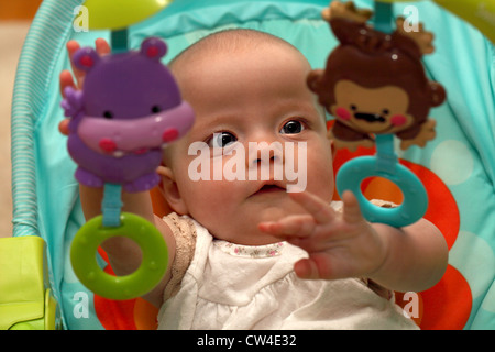 Ein sechs Monate altes Baby versucht, mit ihrem Babystuhl befestigt-Handys spielen Stockfoto