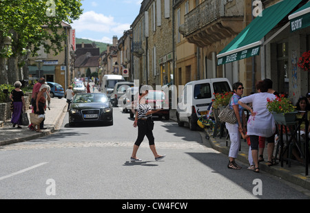 Frau trägt ein Tablett mit Gläsern auf der anderen Straßenseite, eine Bar im Dorf Cazals in der Menge Region von Südwest-Frankreich Stockfoto