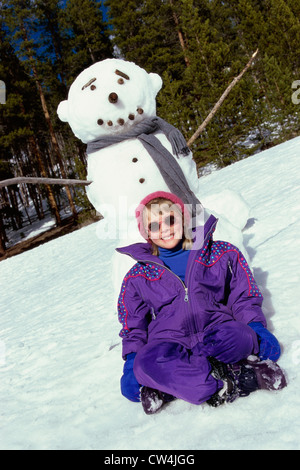 Mädchen sitzen vor einem Schneemann Stockfoto