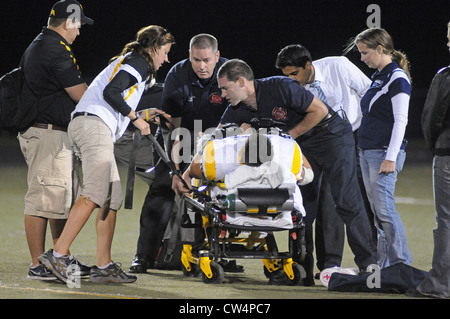 Fußballspieler mit gebrochenen Bein ist vom Feld auf Keilrahmen entfernt nach der ersten Behandlung durch medizinisches Personal während eines Spiels. USA. Stockfoto