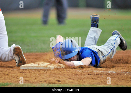 Baseball-Laufsohle taucht zum ersten Base inmitten einer Flut von Schmutz während einer High School Spiels fliegen. Stockfoto