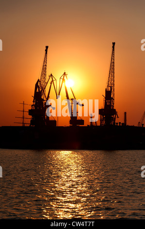 Silhouetten der Hafenkräne gegen eine Sonnenscheibe bei Sonnenuntergang. Die Hafenstadt Odessa, Nachlauf Hafen. Ukraine. Stockfoto