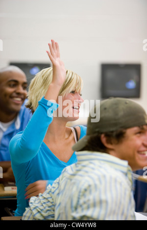 Fröhliche Schüler besuchen Vortrag während einer Studentin hob ihre Hand im Klassenzimmer Stockfoto