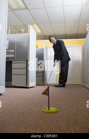 Junger Mann in vollständigen Anzug Golfspielen in einem Büro Stockfoto