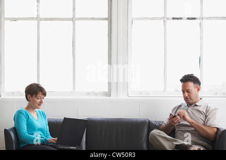 Geschäftsfrau, die Arbeiten auf einem Laptop mit einem Geschäftsmann mit dem PDA Stockfoto