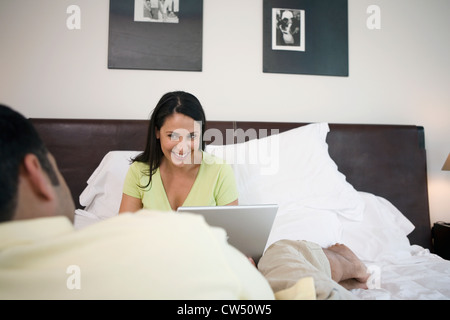 Reife Frau sitzt vor einem reifen Mann mit einem Laptop im Bett Stockfoto