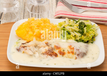 Geräuchertes Kabeljaufilet in einer Käse und Petersilie-Sauce, serviert mit Kartoffeln, Karotten und Schwede Maische mit Kohl Stockfoto