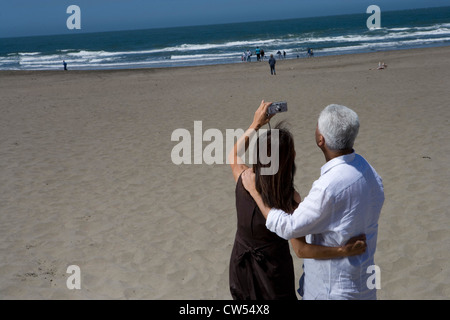 Rückansicht des ein älteres paar fotografieren mit einer digitalen Kamera am Strand Stockfoto