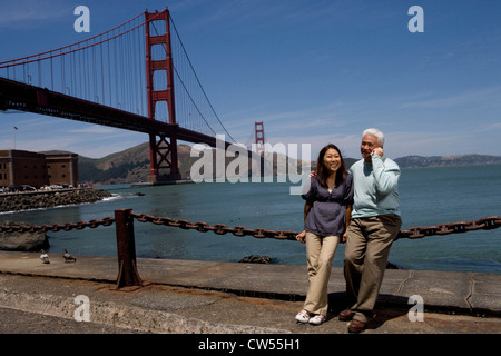 Reife Frau gelehnt Kette mit reifer Mann telefonieren mit Handy Golden Gate Brücke San Francisco Kalifornien, USA Stockfoto