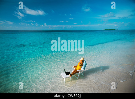 Frau sitzt am Tisch mit Laptop und Handy am Strand während der tropischen Insel Ferien Kombination von Arbeit und Vergnügen Stockfoto