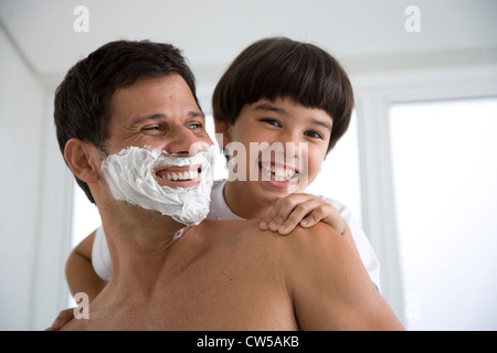 Reifer Mann rasieren und sein Sohn hinter ihm stehen und Lächeln Stockfoto