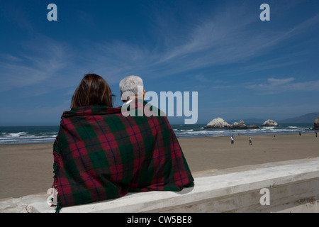 Rückansicht des ein älteres paar eingewickelt in eine Decke am Strand Stockfoto