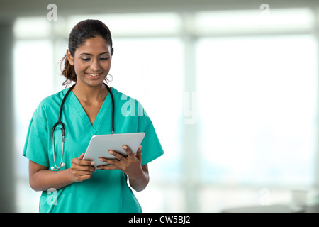 Indische Ärztin Blick auf eine digital-Tablette & tragen scheuert sich ein grünes plus Stethoskop. Stockfoto