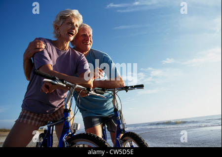 Älteres Paar auf dem Fahrrad sitzen und Lächeln am Strand Stockfoto